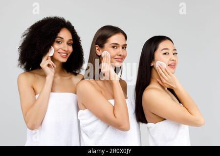 Concept de soin du visage. Jeunes trois différentes dames dans des serviettes en coton, nettoyage de la peau du visage, fond gris Banque D'Images