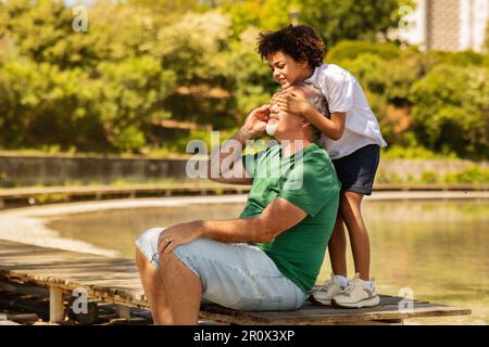 Positif petit enfant noir ferme les yeux à l'ancien grand-père caucasien, aime le temps libre, s'amuser près du lac Banque D'Images