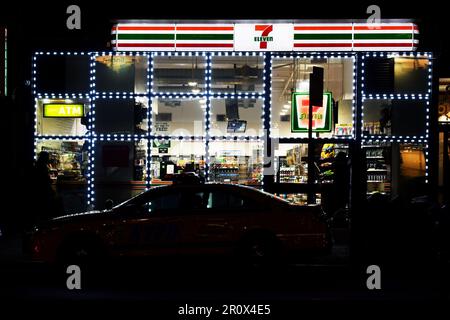Épicerie de proximité 7-Eleven éclairée la nuit avec une voiture garée devant - Scène de rue New York City - États-Unis Banque D'Images