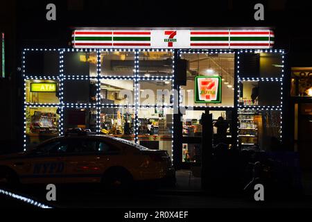 Épicerie de proximité 7-Eleven éclairée la nuit avec une voiture garée devant - Scène de rue New York City - États-Unis Banque D'Images