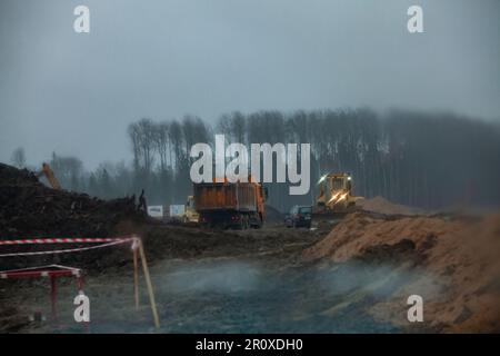 Ust-Luga, oblast de Leningrad, Russie - 16 novembre 2021: Image floue. Chantier de construction de routes en automne et soirée pluie. Bulldozer et tombereau à benne basculante en marche Banque D'Images