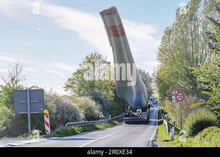 Transport lourd d'une pale d'éolienne levé pour éviter les obstacles et ralentir la circulation sur une route de campagne étroite, industrie pour l'énergie renouvelable, Banque D'Images