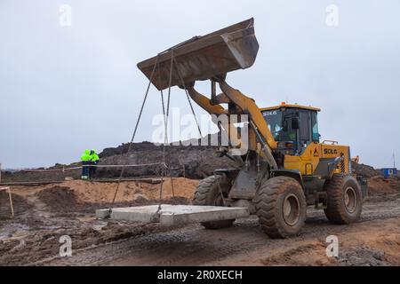 UST-Luga, oblast de Leningrad, Russie - 16 novembre 2021: Bulldozer transportant des tôles de béton à la construction routière Banque D'Images