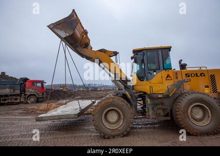 UST-Luga, oblast de Leningrad, Russie - 16 novembre 2021: Bulldozer transportant des tôles de béton à la construction routière Banque D'Images