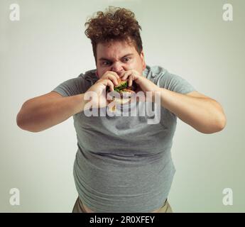 Nothing beats a good burger. Studio shot of an overweight man biting into a burger. Stock Photo