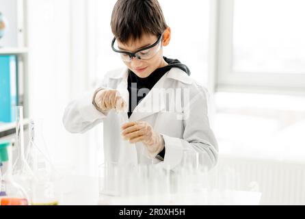 Garçon d'école portant des lunettes de protection faisant une expérience de chimie en classe de sciences élémentaires.Pupille avec tubes d'équipement en laboratoire Banque D'Images