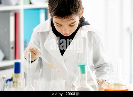 Garçon d'école faisant l'expérience de chimie mesurer des liquides chimiques dans la classe de sciences élémentaires. Pupille intelligente analysant les résultats des tests en laboratoire Banque D'Images