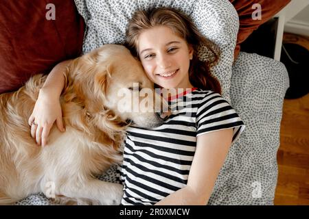 Jolie fille embrassant le chien Golden Retriever et allongé dans le lit. Adolescente avec chien de race purerouge labrador se reposant ensemble Banque D'Images