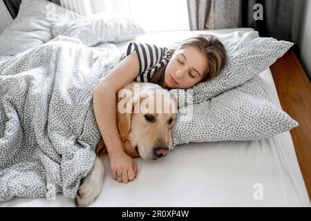 Jolie fille embrassant le chien Golden Retriever et dormant dans le lit. Adolescente avec un chien de race purerouge labrador qui se repose entre eux Banque D'Images