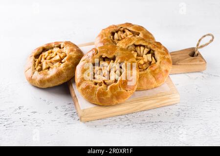 Mini-chaussons doux avec pommes et cannelle sur une planche de bois sur fond gris clair. Délicieux plats faits maison Banque D'Images