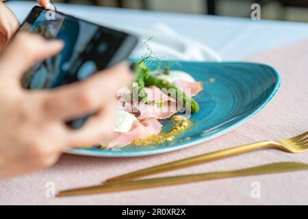 Apéritif avec jambon de romarin, asperges, arachides et taleggio sur la plaque bleue. Une femme prenant une photo de la nourriture avec un téléphone portable. Banque D'Images