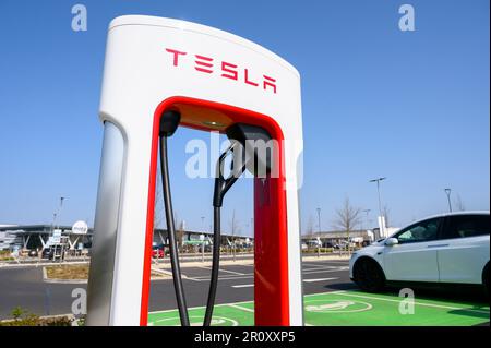 Les voitures Tesla se chargent à des superchargeurs Tesla dans une station-service d'autoroute en Angleterre. Banque D'Images