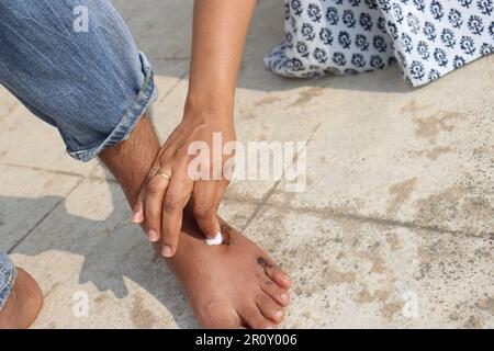 Nettoyer la plaie semi-séchée sur les pieds d'un homme avec du coton avant d'appliquer la pommade avec soin et affection. Concept de premiers soins. Banque D'Images