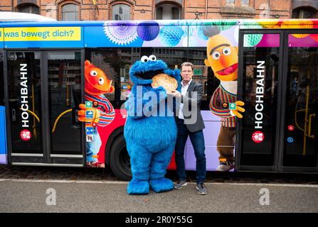 Hambourg, Allemagne. 10th mai 2023. Une personne vêtue d'un monstre de cookie (l) et Raimund Brodehl, Président de l'Association des transports de Hambourg (hvv), se tient devant un bus ferroviaire élevé de Hambourg, qui a les personnages Ernie (l) et Bert collés dessus pour marquer le 50th anniversaire de Sesame Street. Credit: Daniel Bockwoldt/dpa/Alay Live News Banque D'Images