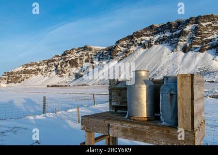 Vue rapprochée d'un stand de départ de lait le long de la route en Islande avec quelques canettes de lait pour le lait frais sur fond d'un réseau local montagneux enneigé Banque D'Images