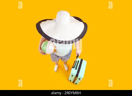 Drôle de photo grand angle de femme avec grand chapeau de soleil, ballon de plage et valise pendant les vacances d'été Banque D'Images