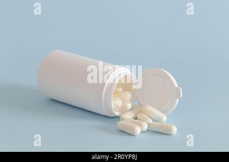 Flacon de médicament blanc avec un couvercle couché avec les capsules tombées sur un fond bleu. Banque D'Images