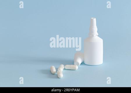 Un flacon de spray nasal avec le bouchon retiré et quelques capsules de médicament placées à côté. Produits blancs sur fond bleu. Horizontale. Banque D'Images