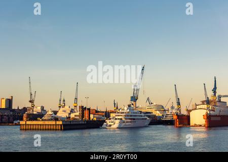 Vue panoramique Grand yacht de luxe moderne au service d'entretien contre les grues de cargaison de construction au quai sec du chantier naval dans le port de Hambourg Banque D'Images