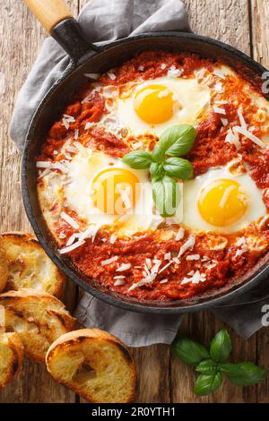 Œufs frits dans une sauce tomate épicée avec oignon et ail arrosé de parmesan dans une poêle à frire sur une table en bois. Vue verticale du dessus de l'ab Banque D'Images