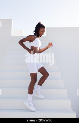 Vue latérale d'une femme mince descendant dans les escaliers à l'extérieur. Pleine longueur de jeune femme de forme physique pratiquant à l'extérieur. Banque D'Images
