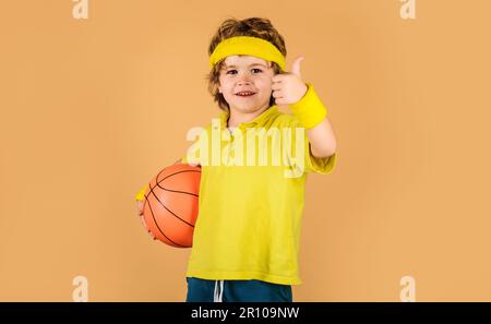 Entraînement au basket-ball. Enfant dans des vêtements de sport avec ballon de basket-ball montrant le pouce vers le haut. Jeu de sport. Style de vie sportif actif. Petit ballon de base avec Banque D'Images