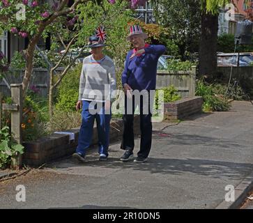 Des femmes âgées qui marchent sur le trottoir discutant avec Union Jack sur les chapeaux de la Street Party célébrant le Roi Charles III Coronation Surrey Angleterre Banque D'Images