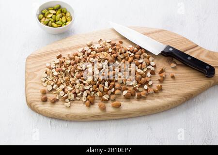 Planche en bois avec noisettes et amandes hachées et un bol de pistaches pelées sur fond gris clair. Étape de cuisson délicieux desseur maison Banque D'Images