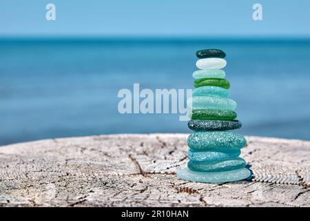 Une pyramide équilibrée de bouteilles de verre polies sur une surface en bois abîmée sur fond de mer. Méditation par l'océan Banque D'Images