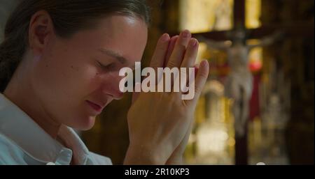 Une fille adulte a labouré sa tête dans la prière d'action de grâce à Dieu dans l'église. La jeune femme a plié les mains dans la prière au Christ Rédempteur. Vue rapprochée du cinéma. Banque D'Images