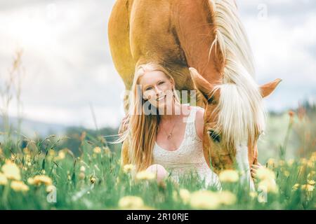 Une jeune femme blonde et son cheval haflinger appréciant leur temps au printemps dehors. Scène d'amitié entre une équestrienne et son poney Banque D'Images