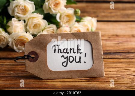 Étiquette avec phrase Merci et roses sur table en bois, gros plan Banque D'Images