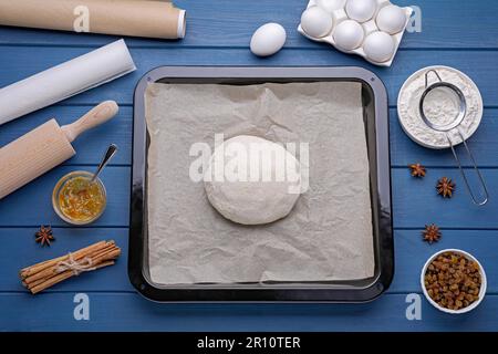 Moule à pain avec pâte, papier parchemin et ingrédients sur table en bois bleu, plat Banque D'Images