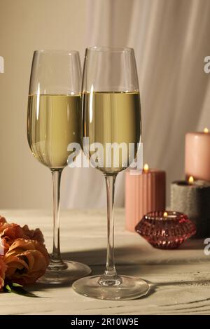 Verres de vin mousseux, fleurs et bougies allumées sur table blanche Banque D'Images