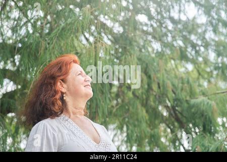 Portrait d'une femme latino-américaine aux cheveux rouges souriant, rêvant de rêver dans la nature. Composition lumineuse avec espace de copie. Concept: La paix de l'esprit et h Banque D'Images