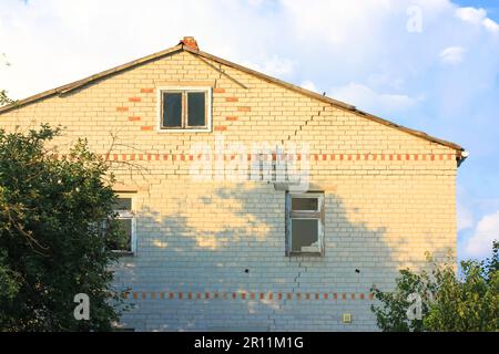 Une maison de deux étages en brique blanche avec une fissure à travers toute la façade contre un ciel bleu le jour d'été du printemps. Bâtiment résidentiel en brique blanche avec Banque D'Images