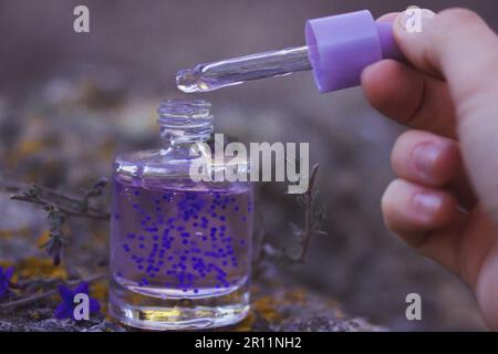 Flacon compte-gouttes en verre transparent cosmétique, pipette pour main femelle sérum violet violet pour hydrater la peau du visage. Cosmétiques naturels, produits de beauté. C Banque D'Images