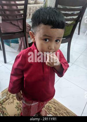 Malaisie, 10 mai 2022 : un garçon soigné portant une chemise malaise rouge le matin de Hari Raya (en malay) Banque D'Images