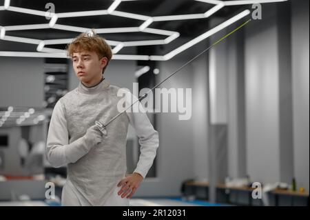 Portrait d'un tireur d'adolescents portant un costume blanc d'escrime avec une épée Banque D'Images