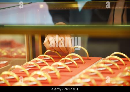 RENHUAI, CHINE - 11 MAI 2023 - Un membre du personnel choisit un bracelet or pour un client dans une boutique d'or à Renhuai, dans la province de Guizhou, au sud-ouest de la Chine Banque D'Images