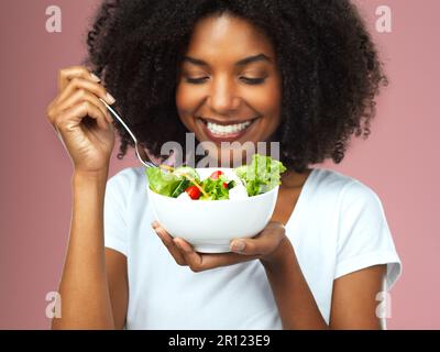 Mangez bien, sentez bien. Photo en studio d'une jeune femme attrayante qui mange de la salade sur fond rose. Banque D'Images