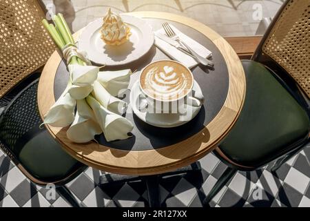 Cappuccino, délicieux dessert à la crème fouettée et fleurs de cala blanches sur une table en bois dans le café. Maquette pour café ou restaurant. Concept amour et romance. Banque D'Images