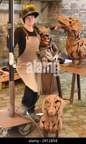 PRODUCTION - 05 mai 2023, Saxe, Leipzig: L'artiste sidérurgique Dana Meyer se tient dans son arrière-cour par deux dachshunds de 1,10 mètres de long, qui fait partie de son studio, dans le cadre d'une nouvelle installation. Avec de plus petits insectes métalliques dans le verre, les sculptures en acier de taille réelle inhabituelles sont parmi les œuvres que l'artiste forge à main levée et sans dessins en plastique. Elle utilise principalement des plaques d'acier pour créer des pièces forgées, qu'elle assemble dans des figures inhabituelles comme un puzzle à l'aide d'un chalumeau de découpe et d'un équipement de soudage. Elle est représentée avec ses œuvres de 12,5.-20.08.23 à la Galerie Rothamel à Frankfur Banque D'Images