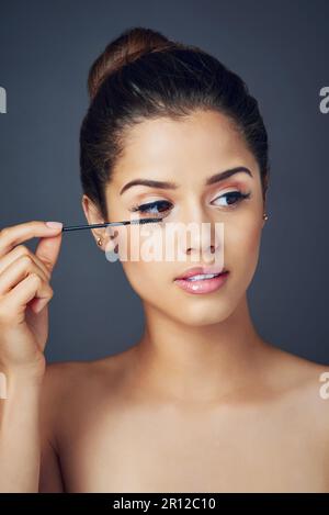 Faire de ses yeux la principale attraction. Studio photo d'une belle jeune femme appliquant la mascara tout en posant sur un fond bleu. Banque D'Images