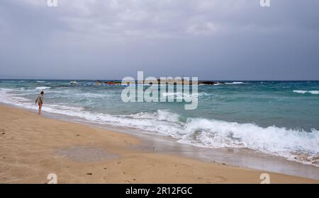 Personne non reconnue qui marche sur une plage de sable tropical. Activités de plein air. Vagues venteuses et orageuses. Banque D'Images