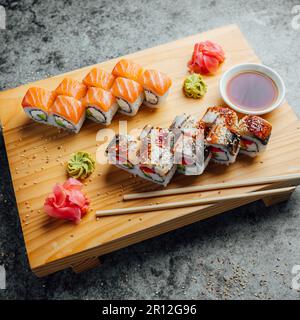 Une sélection de petits pains à sushis sur une planche à découper en bois, servis avec une paire de baguettes Banque D'Images