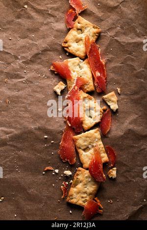 Viande jerky avec craquelins croustillants sur fond de papier brun, vue du dessus. Banque D'Images