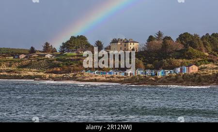 Une vue imprenable sur un arc-en-ciel vibrant qui s'étend sur une rangée de maisons situées près d'une côte tranquille Banque D'Images