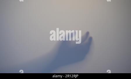 Ombre flou d'un homme d'horreur derrière le verre dépoli. Main floue, abstraction de la forme du corps et une paume. Reflet de la silhouette à travers la lumière. Banque D'Images