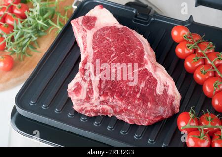 Steaks de première qualité crus sur le gril électrique. Steaks de viande de choix black angus Ribeye sur un grill électrique moderne au romarin, à la tomate cerise et au poivre. Cuisine pro Banque D'Images